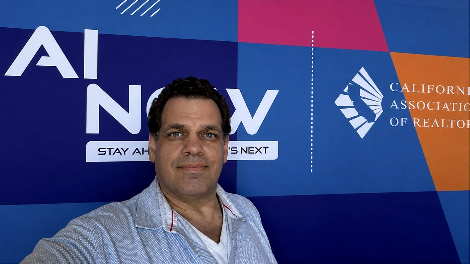 Thomas Fraley standing in front of the blue AI NOW event backdrop in Fresno