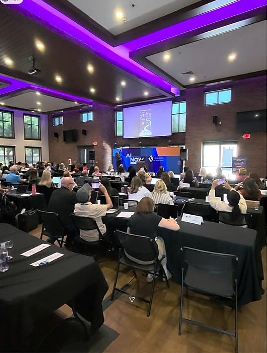 Wide view of the AI NOW Fresno audience seated with laptops and mobile devices during the program