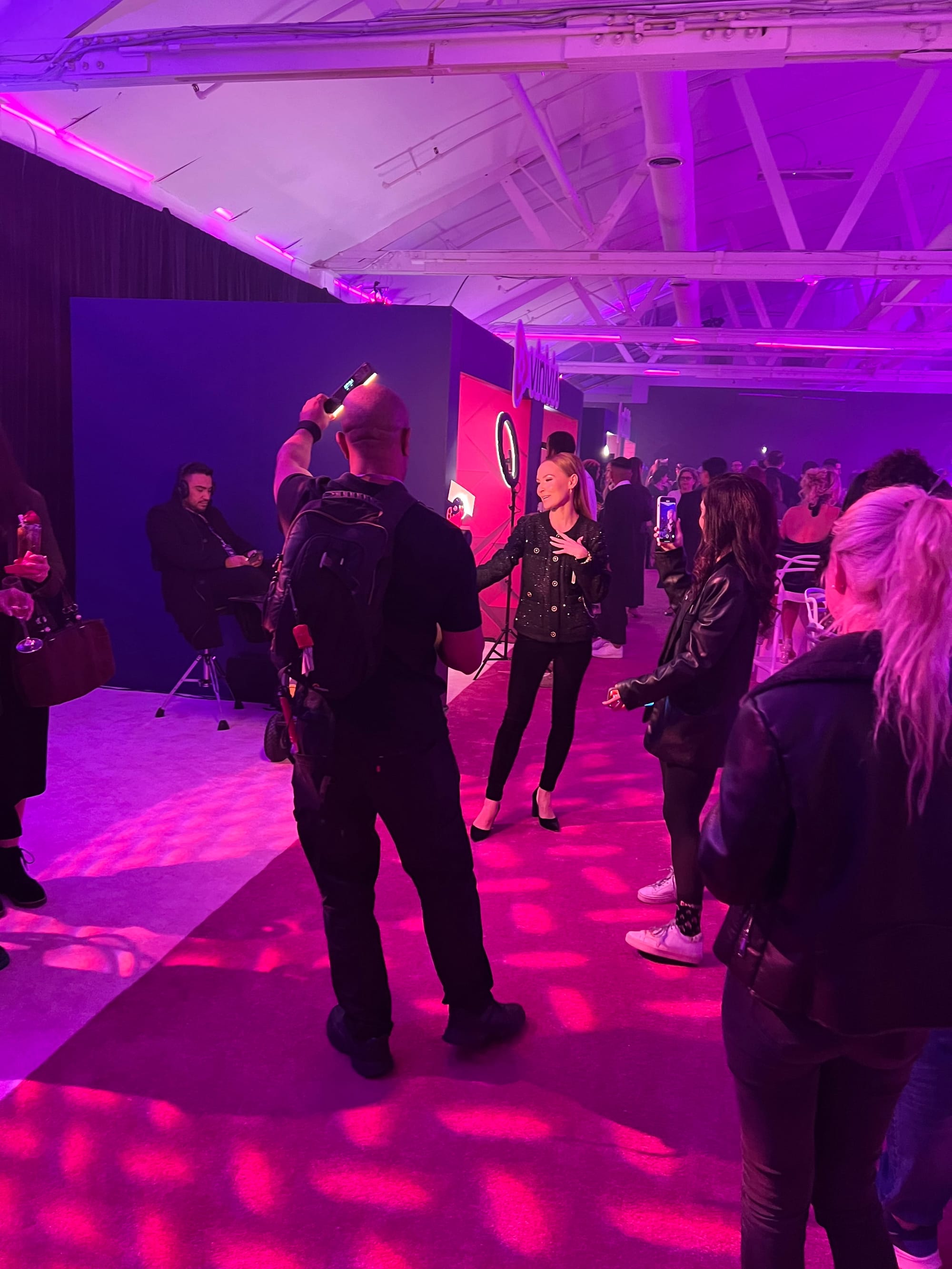 Guests and production crew moving through the magenta-lit event floor
