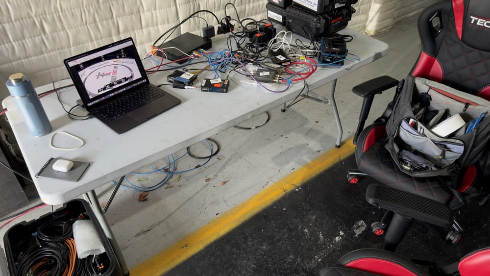 A compact live-production workstation with a laptop, network cabling, converters, and field equipment at an LXF event